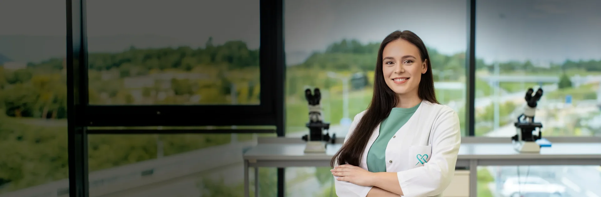 Moteris su baltu chalatu stovi laboratorijoje