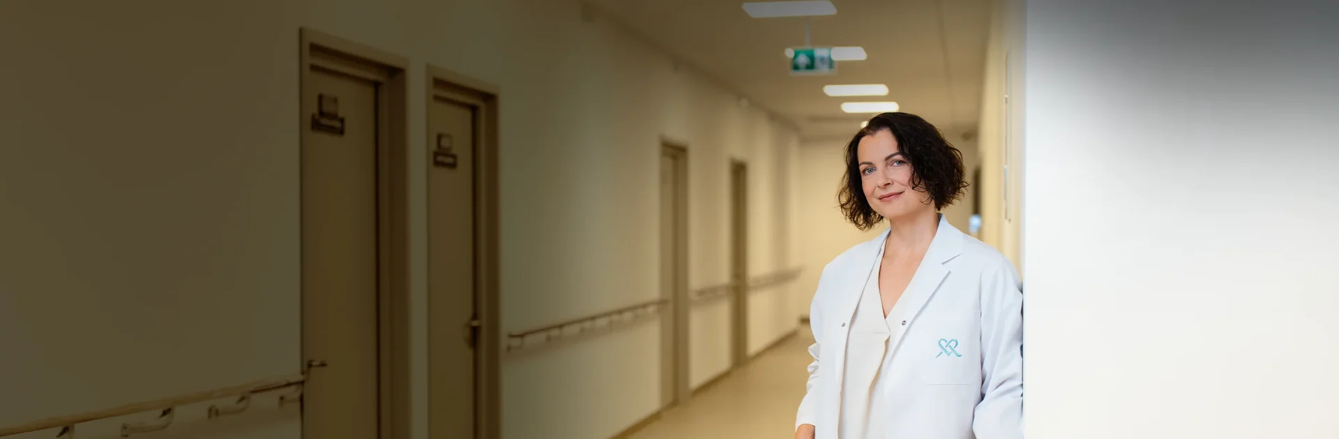 Gydytoja su baltu chalatu stovi koridoriuje klinikoje